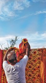 Rear view of man holding plants against sky
