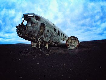 Old rusty abandoned airplane on beach against sky