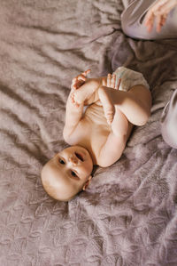 Cute baby in a diaper is lying on the bed on his back and holding his legs