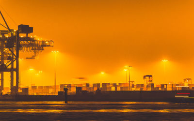 Illuminated buildings by sea against sky during sunset