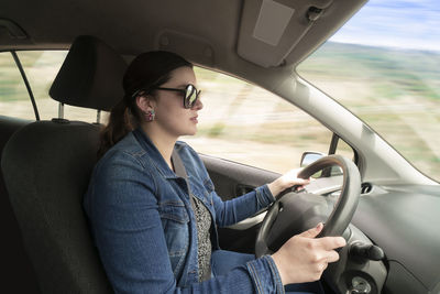 Side view of young latin woman dressed in blue with glasses driving her car at high speed