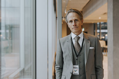 Portrait of confident mature businessman standing by window at office