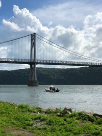 Suspension bridge over river against cloudy sky