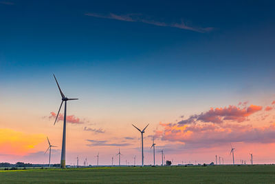 Windmills on field against sky during sunset
