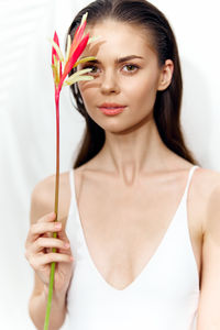 Portrait of young woman holding red rose against white background
