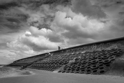 Retaining wall at beach against cloudy sky