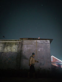 Man standing by building against sky at night