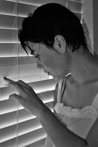 Side view of young woman peeking through window at home