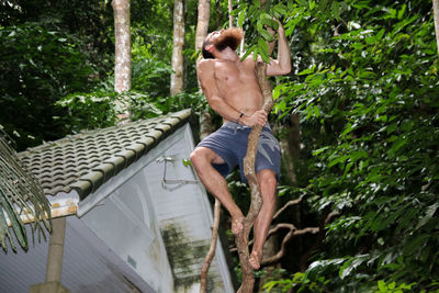 Low angle view of shirtless man climbing on tree