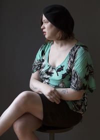 Woman looking away while sitting against gray background