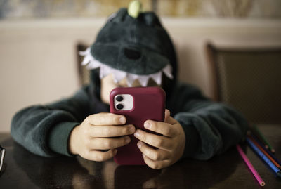 Boy who looks into the phone sitting in a dinosaur costume at the table. unrecognizable face