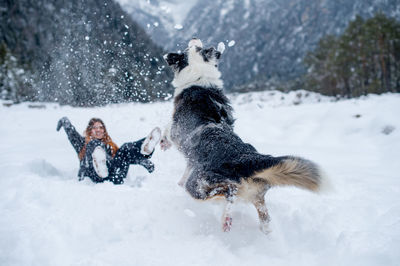 Cheerful woman playing with dog on snow covered field