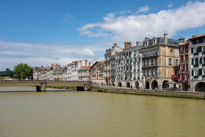 Bridge over river by buildings in town against sky