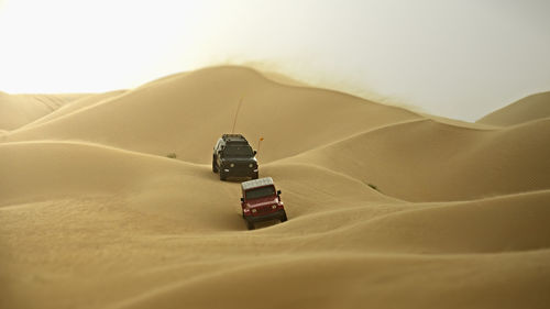 Vehicles on sand dunes in desert against sky