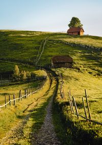 Scenic view of empty country road and house on hill against sky in summer