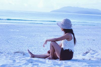 Woman sitting at beach against sky