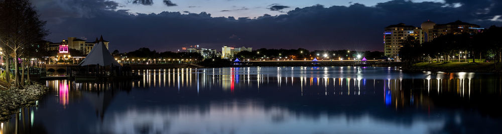 Illuminated buildings by river against sky at night