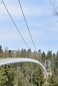 Suspended bridge over forest against sky