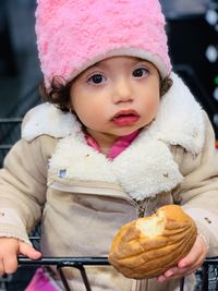 Portrait of cute girl eating bread while sitting in shopping cart