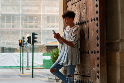 Young afro leaning on a wooden gate looking at his phone