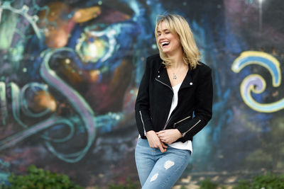 Young woman laughing while standing against graffiti wall