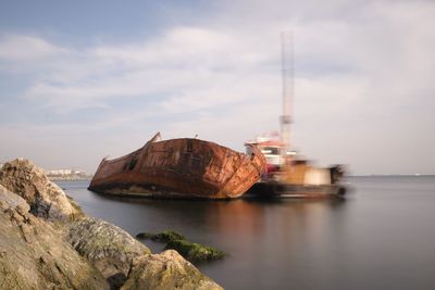 Abandoned boat on sea against cloudy sky