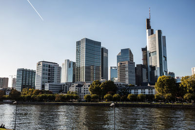 Modern buildings by river against sky in city