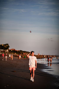 Rear view of people standing on beach against sky during sunset