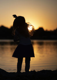 Silhouette woman standing on beach against sky during sunset