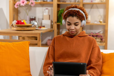 Young woman using digital tablet while sitting on sofa at home