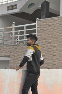 Side view of young man standing against brick wall