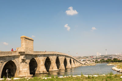 Arch bridge over river against sky in city