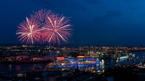 Firework display over illuminated city against sky at night