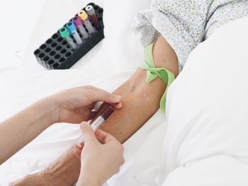 Cropped hand of doctor holding syringe by patient hand on bed at hospital