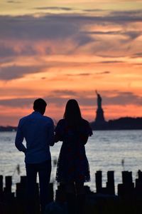 Rear view of silhouette couple standing against sea during sunset