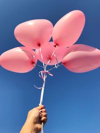 Low angle view of cropped hand holding balloons against clear blue sky