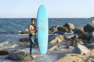 Full length of man standing with surfboard against sea