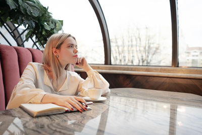 Young woman looking away while sitting on table