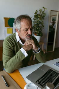 Man with hand on chin using laptop while sitting at home