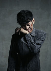 Injured young man crying while standing against wall