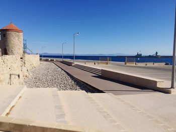 Footpath by sea against clear blue sky