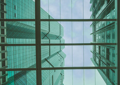 Directly below shot of modern buildings against sky seen through glass window