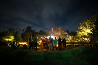 People at illuminated park against sky at night