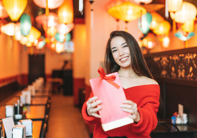 Beautiful young asian woman in red clothes with red gift bag in restaurant celebrating chinese 