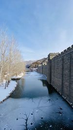 Frozen canal amidst buildings against sky during winter
