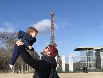 Father catching while playing with son against eiffel tower and sky