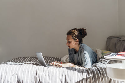 Woman using laptop while lying on bed at home