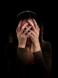 Depressed woman covering face against black background