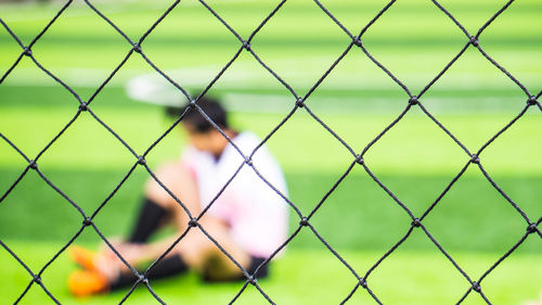 Male soccer player sitting on field seen through net