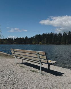 Empty bench by lake against sky